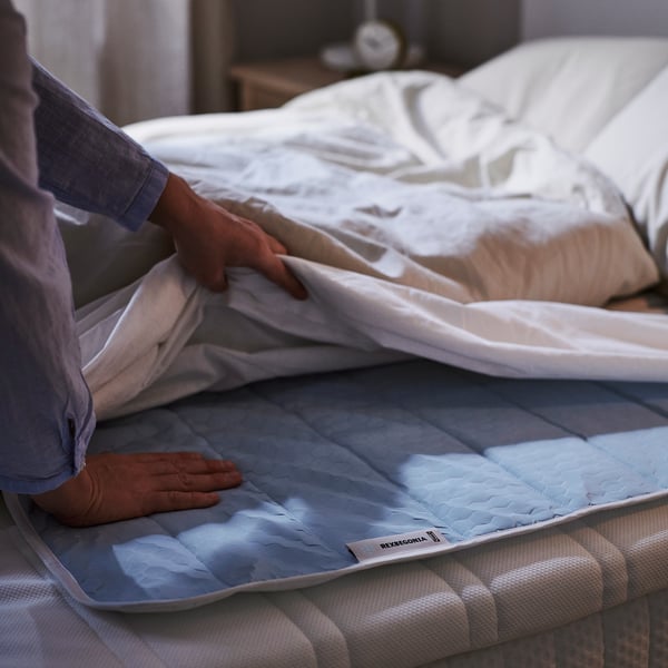 Person placing blue REXBEGONIA cooling pad on bed for comfortable sleep.