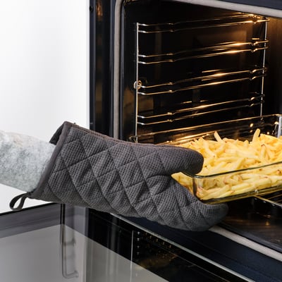 Person wearing grey RINNIG gloves placing tray of food into oven. Gloves protect hands from heat.