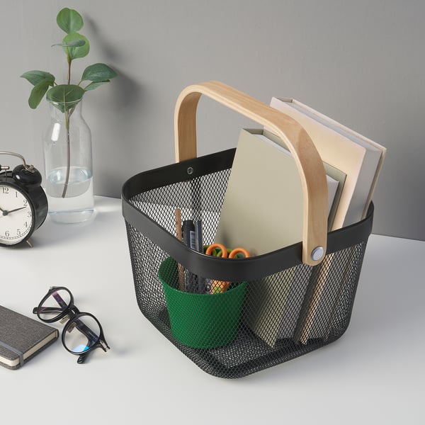 Black mesh storage basket with wooden handle holds office supplies, including notebooks, pens, and scissors.