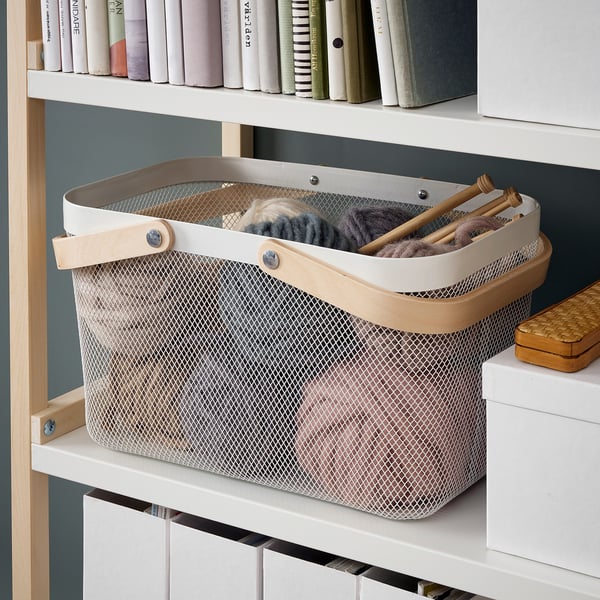 Large storage basket with handles holds knitting supplies on shelf.