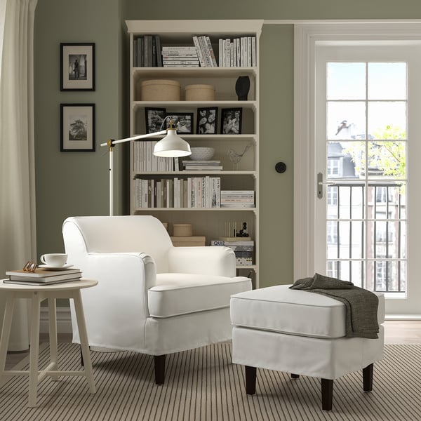 Cosy green room with white ROCKSJÖN armchair and footstool, striped rug, bookshelf, and lamp. Perfect for small spaces.