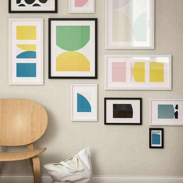 Room with colourful abstract art, white & dark frames. Wooden chair with pillow. Prominent RÖDALM frame.