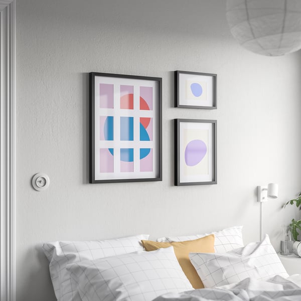 Three colourful abstract art frames above bed in minimalist room.