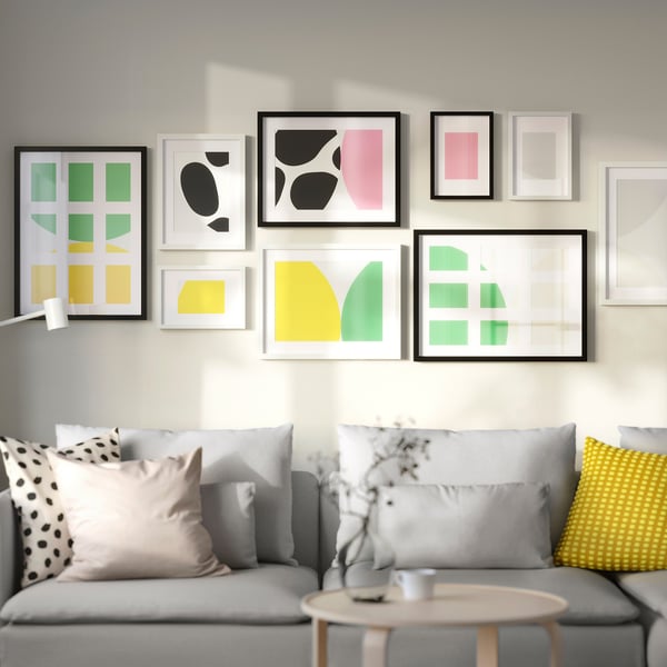 Modern living room with colourful pillows on grey sofa and black RÖDALM frames displaying art in varied sizes.