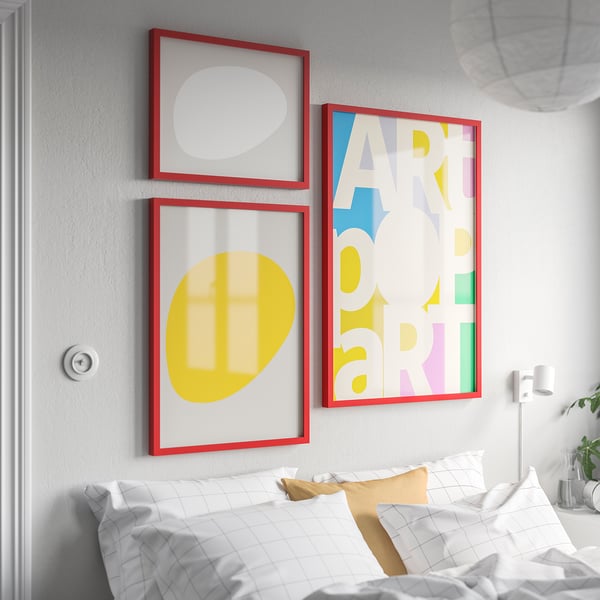 Three RÖDALM red frames above bed: art party, yellow & white abstract, gold pillow.