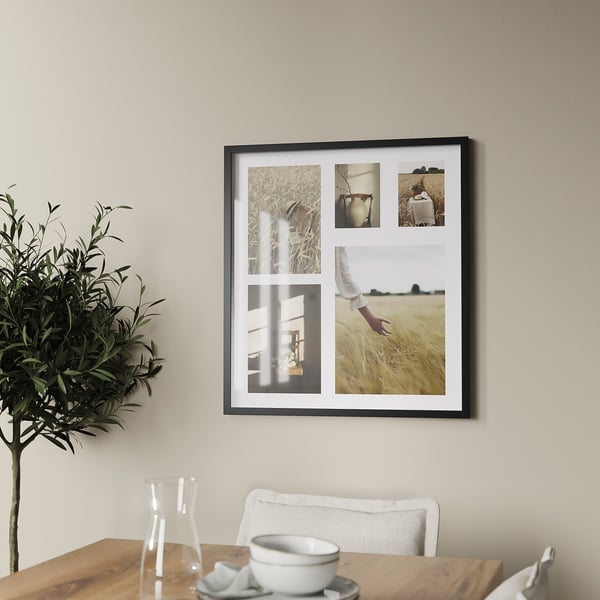 A wall-mounted picture frame, larger than a chair, displays four photos inside. Its black frame contrasts with the light-colored wall.