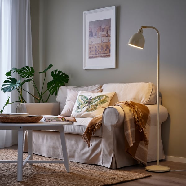 Cosy living room with RÖDFLIK lamp, beige sofa, pillows, cityscape art, throw blanket, coffee table, and monstera plant.