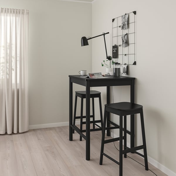 Black bar table with stools in modern room. Rounded corners, sleek surface, matching stools.