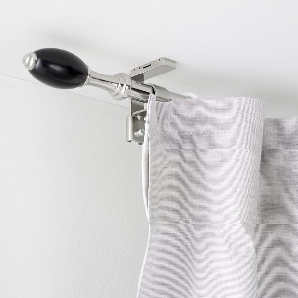 Black and silver curtain rod with finials mounted on white wall, holding striped curtains.