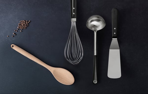 Kitchen utensils: black whisk, wood spoon, metal ladle, spatula on dark background. Modern minimalist design.