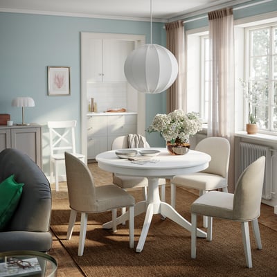 Light blue dining room with white extendable table, beige chairs on jute rug, and pendant light.