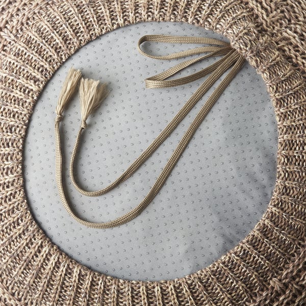 Hand-woven pouch with two long handles and tassels, laid on a grey fabric background.