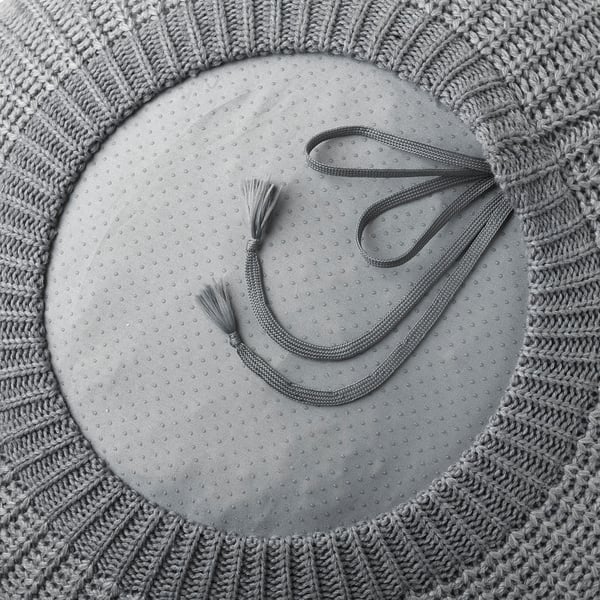 Grey crochet pouffe with tassel ties, doubling as a footstool or extra seat, shown in circular form.