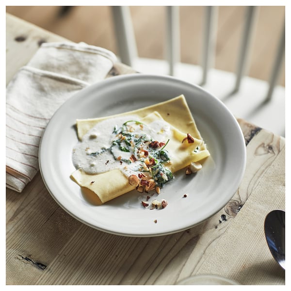 Plate of folded crepe with spinach, sauce, and nuts on wooden table.