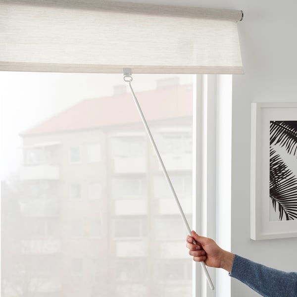 Person lowers cordless beige roller blind on white window frame for light filtering and privacy.