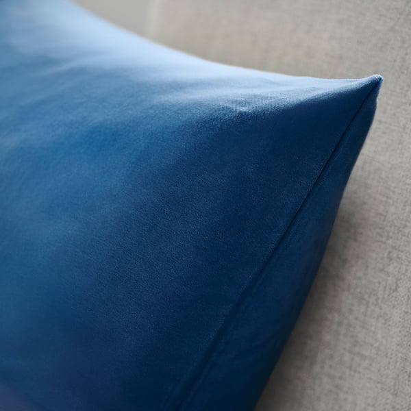 Blue velvet cushion on grey fabric. Soft, high-quality material with visible stitching.