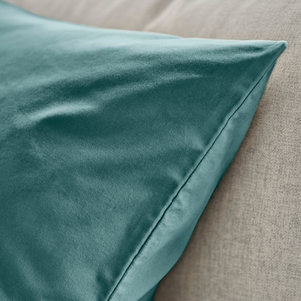 Teal velvet cushion on beige fabric, smooth texture, visible stitching detail.