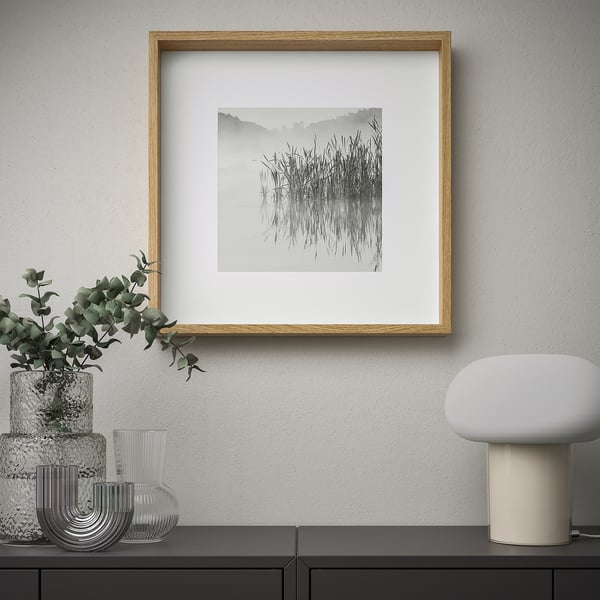 A minimalist wall display featuring a framed black-and-white nature photo, surrounded by decorative vases and a modern lamp.