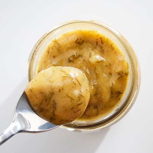 A jar of yellow mustard and dill sauce, with a spoonful lifted out.