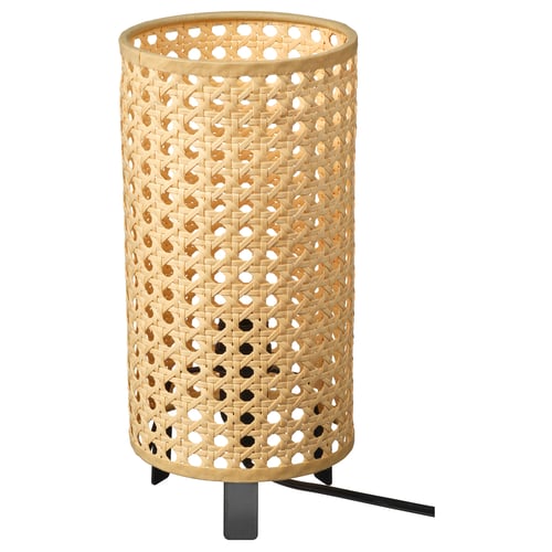 The SAXHYTTAN lamp has a beige, woven paper shade with a cylindrical shape. It sits on a black metal base and casts warm light with playful shadows.