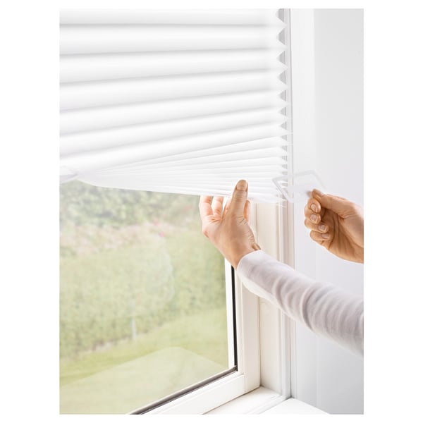Person adjusting white window blinds, securing with clips, ensuring privacy and reducing glare.