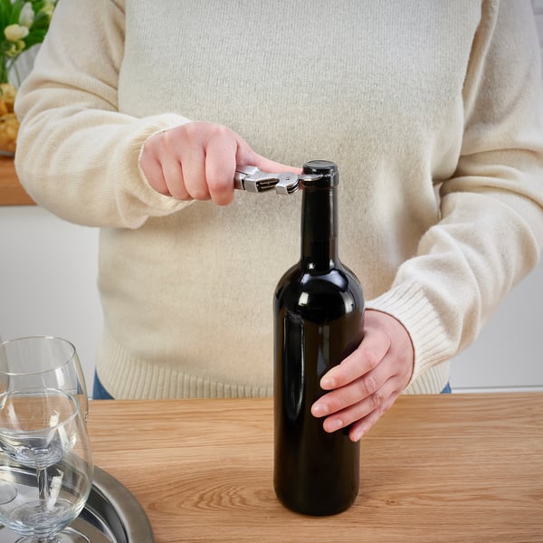 Person using corkscrew to open wine bottle on table.