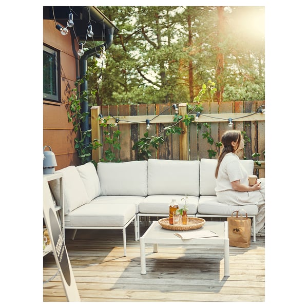 Person relaxes on SEGERÖN patio sofa with solar lights, plants, and a bag.