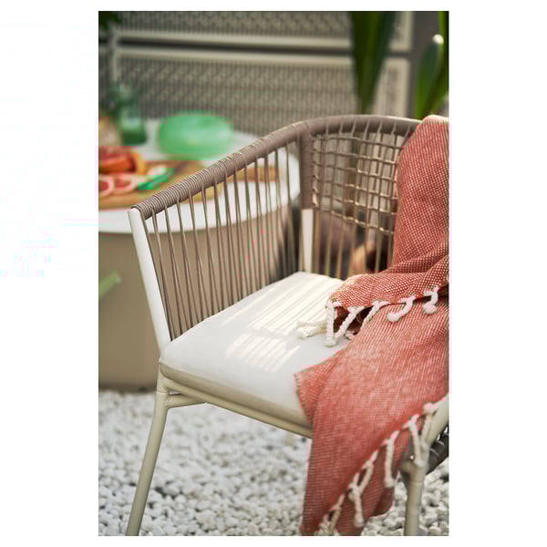 Modern outdoor chair with woven back, white cushion, red blanket, on white pebbles.