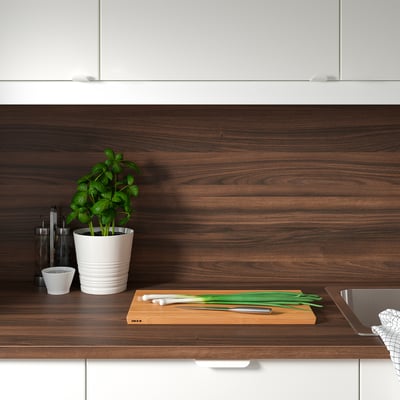 Modern kitchen with dark brown wooden countertop, white cabinets, sink, green plant, and cutting board with scallions.
