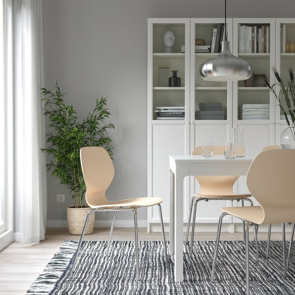 Cosy dining area with wooden chairs, small table, bookcase, pendant light, rug, and plant.