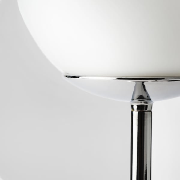 Close-up of sleek chrome lamp base supporting elegant, round glass shade.