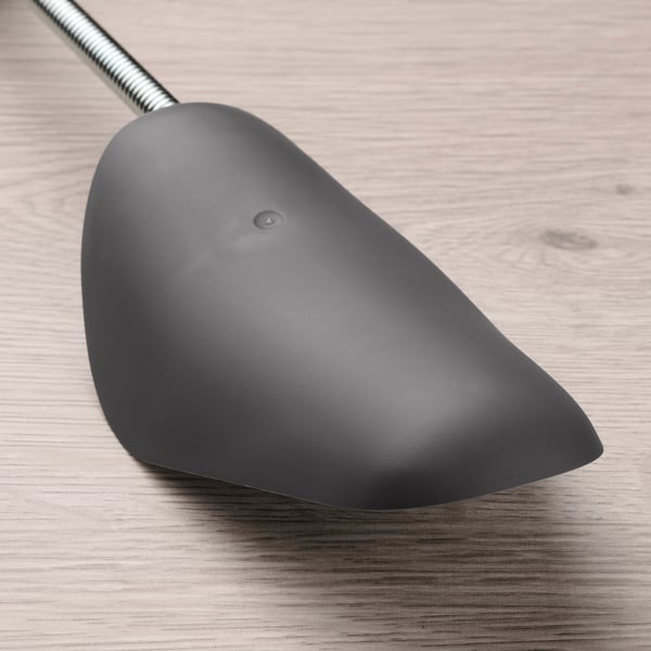 Dark grey shoe shaper with a flexible middle section on a wooden surface.