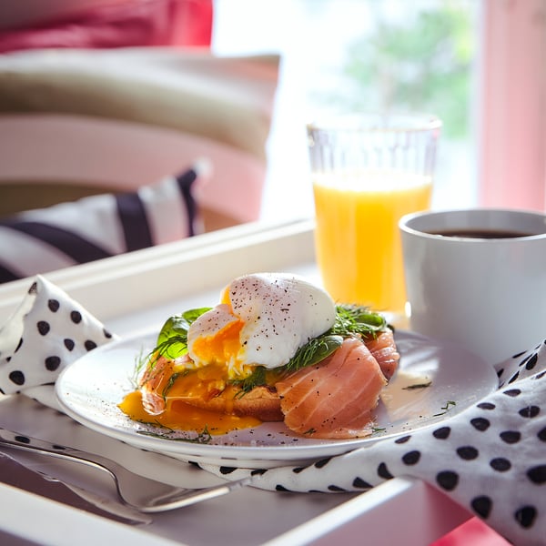 Breakfast of poached egg, salmon, spinach, oj, coffee on tray, pink wall.