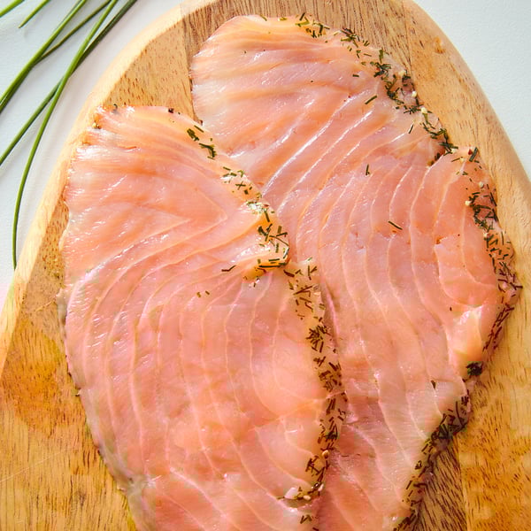 Raw salmon fillets marinated with herbs on a wooden board.