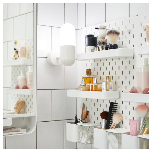 Modern white bathroom with pegboard shelves and toiletries. Two capsule lights.