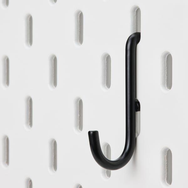 Black metal hook attached to white pegboard, close-up. Simple, sturdy design for organising items.