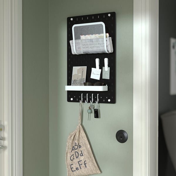 Black SKÅDIS pegboard organises office or home items. Holds notes, keys, and bag.