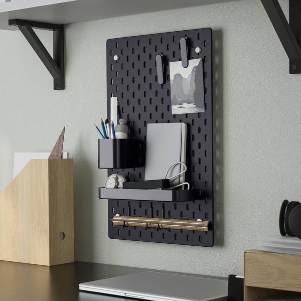 Wall-mounted SKÅDIS organiser with notebook, pens, and a clock.