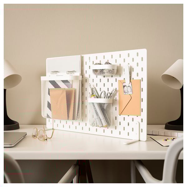 A white SKÅDIS pegboard desk organiser with mesh pockets and a memo holder, holding various office supplies.