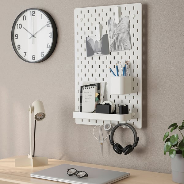 Wall-mounted organiser with clock, lamp, desk items, and plants. SKÅDIS pegboard displays neatly arranged office accessories and decor.