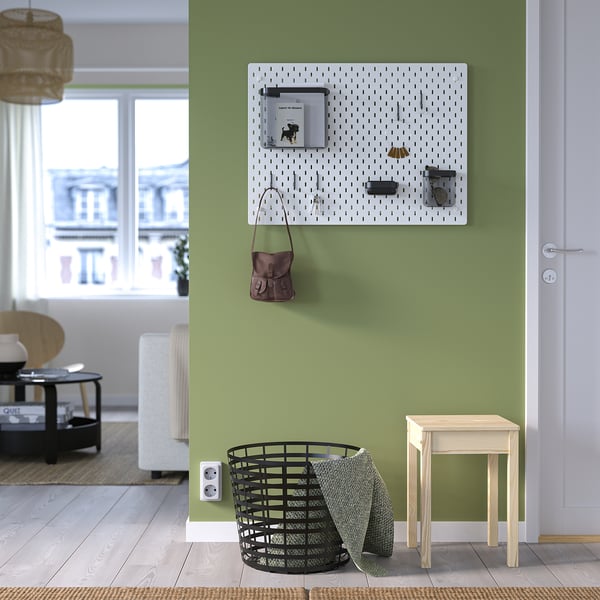 Green wall SKÅDIS pegboard with purse & items, black basket with towels, wooden stool, large windows.