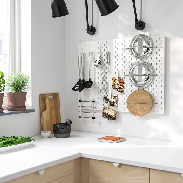 White kitchen with SKÅDIS pegboard, utensils, and spices. Efficient, adjustable storage next to cabinets and plants.