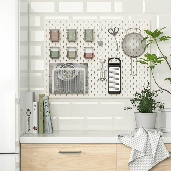 Kitchen pegboard organiser with spices, tools, and plant. Efficient and neat storage solution.