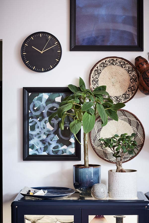 Modern decor: black clock, plants, art, sideboard.