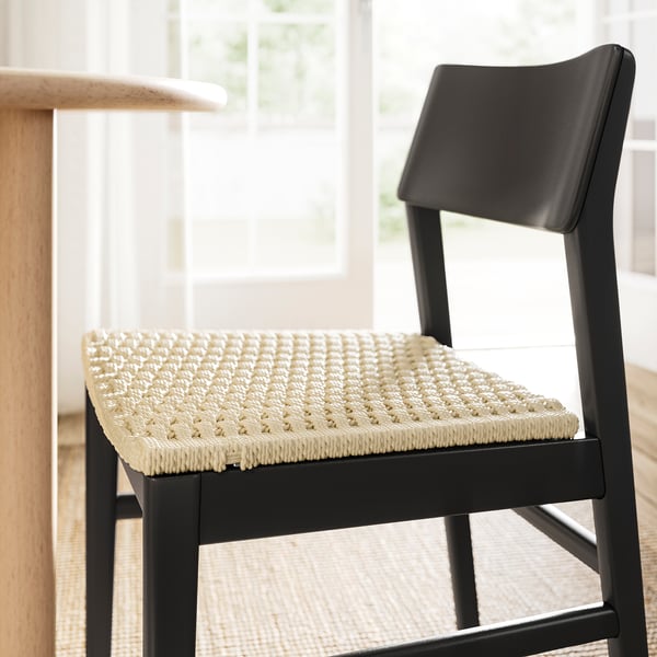 Modern black chair with woven beige seat. Sleek design, smooth back.