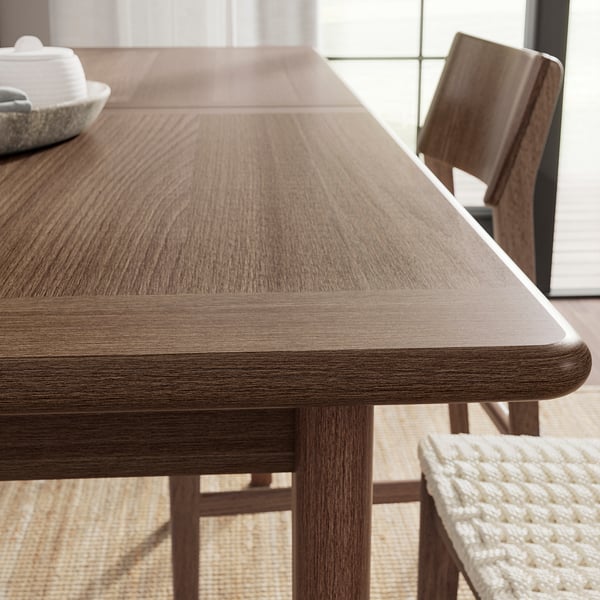 Close-up of a modern, wooden dining table with smooth, layered finish, positioned near a window.