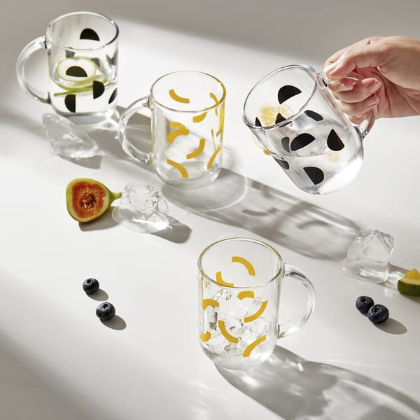 Hand holding a clear glass mug, three others nearby, each with citrus twists and ice. One has blueberries. Table has sliced fruits.