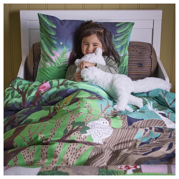 A girl in bed, hugging a stuffed animal, with colourful forest-themed bedding, showcasing durable, soft, and easy-care fabric.