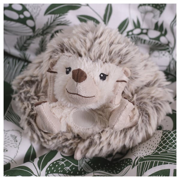 A cuddly toy hedgehog on patterned fabric, soft and detailed, with embroidered and a friendly, inviting smile.