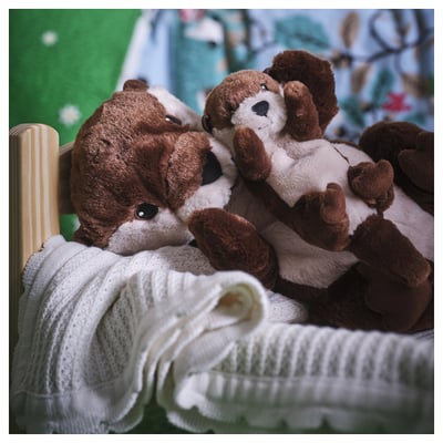 SKOGSDUVA brown/white plush otters nestled with white knit blanket. Soft, huggable, and realistic for children.